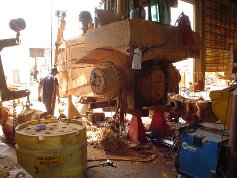 1966 International School Bus - Heavy machinery is undergoing repairs in a workshop, with tools and equipment scattered around.