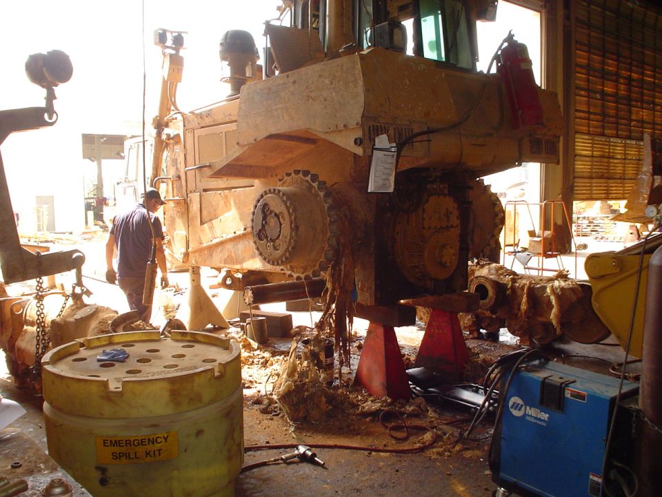 Muddy crawler dozer on jack stands in shop with final drive and sprocket exposed