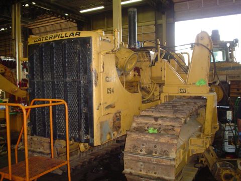 1966 International School Bus - A yellow Caterpillar bulldozer, identified as C94, is seen in a workshop setting with another vehicle partially visible in the background.