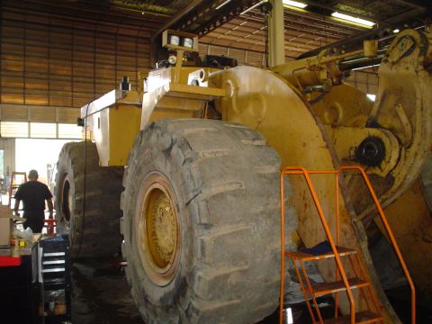 1966 International School Bus - A large yellow loader with massive tires sits in a workshop, with a person in the background.