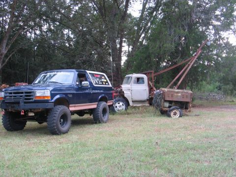 1995 Ford Bronco - A blue Ford Bronco is parked in a grassy area next to an old tow truck and generator.