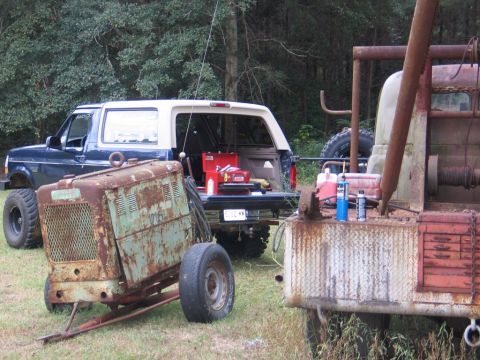 1995 Ford Bronco - A blue 1995 Ford Bronco is parked next to some rusty equipment, with its tailgate open revealing a toolbox.