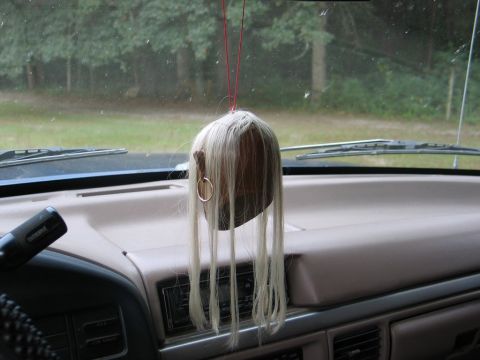 1995 Ford Bronco - A novelty air freshener shaped like a head with blonde hair hangs from the rearview mirror inside a vehicle.