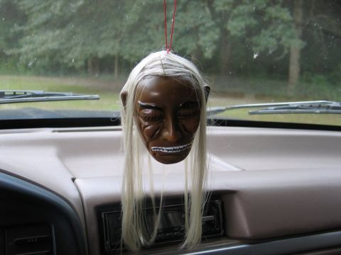 1995 Ford Bronco - A creepy mask with white hair and sharp teeth hangs from the dashboard of a vehicle.