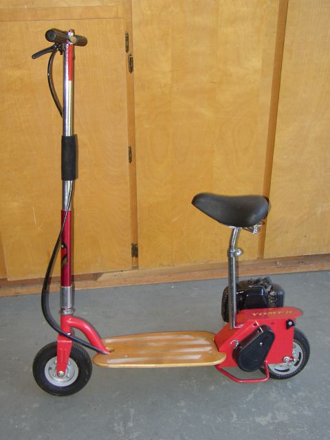 1987 Volkswagen Golf - This red motorized scooter features a wooden deck, a seat, and a visible "YOMER" label on the rear. It is not a 1987 Volkswagen Golf.