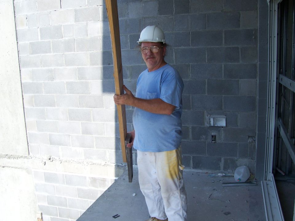 Man in hard hat holding a piece of wood against a cinder block wall