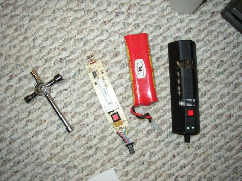 1987 Volkswagen Golf - Electronic components including a circuit board, battery, and a black device with a red button are laid out on a carpeted surface.
