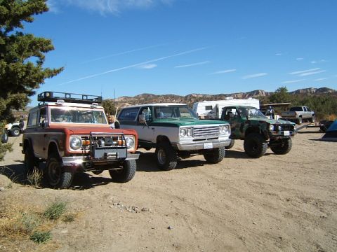 1988 Ford Bronco - Several off-road vehicles are parked at a campsite with a camper trailer and a pickup truck visible in the background.