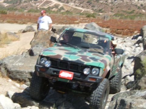 1988 Ford Bronco - Pickup truck with camouflage paint job is driven over large rocks on an off-road trail.