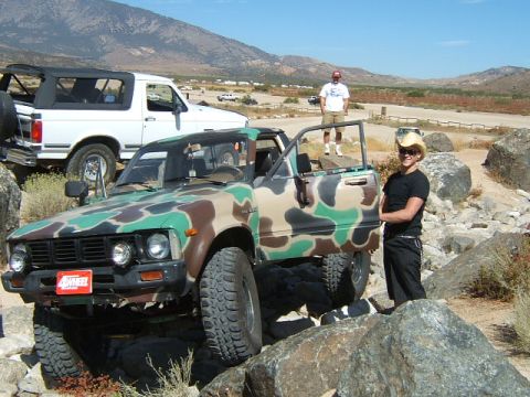 1988 Ford Bronco - A camouflage pickup truck is parked on a rocky trail with a white SUV in the background.
