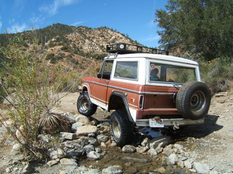 1988 Ford Bronco - This SUV navigates a rocky stream bed on a dirt trail, with a spare tire mounted on the rear.
