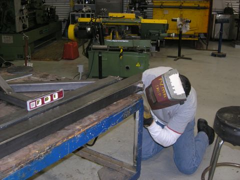 2001 Jeep Wrangler - A person welds a metal frame in a workshop setting, with machinery in the background.