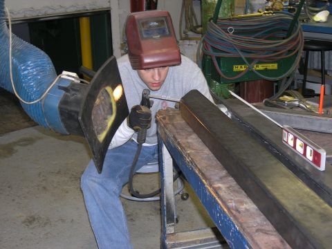 2001 Jeep Wrangler - A person wearing a welding helmet and protective gear works on a metal beam, with welding equipment and tools visible in the background.