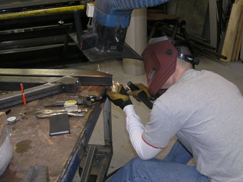2001 Jeep Wrangler - A person welds metal components on a workbench, surrounded by tools and equipment.