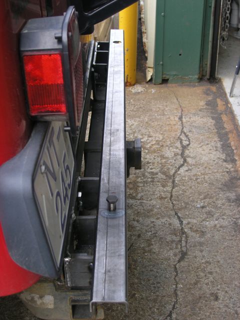 2001 Jeep Wrangler - A close-up view of a red vehicle's rear bumper, showing a custom metal modification and license plate.
