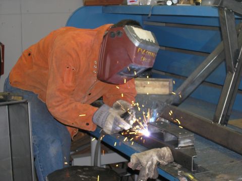 2001 Jeep Wrangler - A welder works on a metal frame in a workshop, with sparks flying.