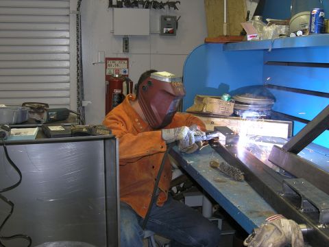 2001 Jeep Wrangler - A person is welding metal parts in a workshop setting, with tools and equipment visible.