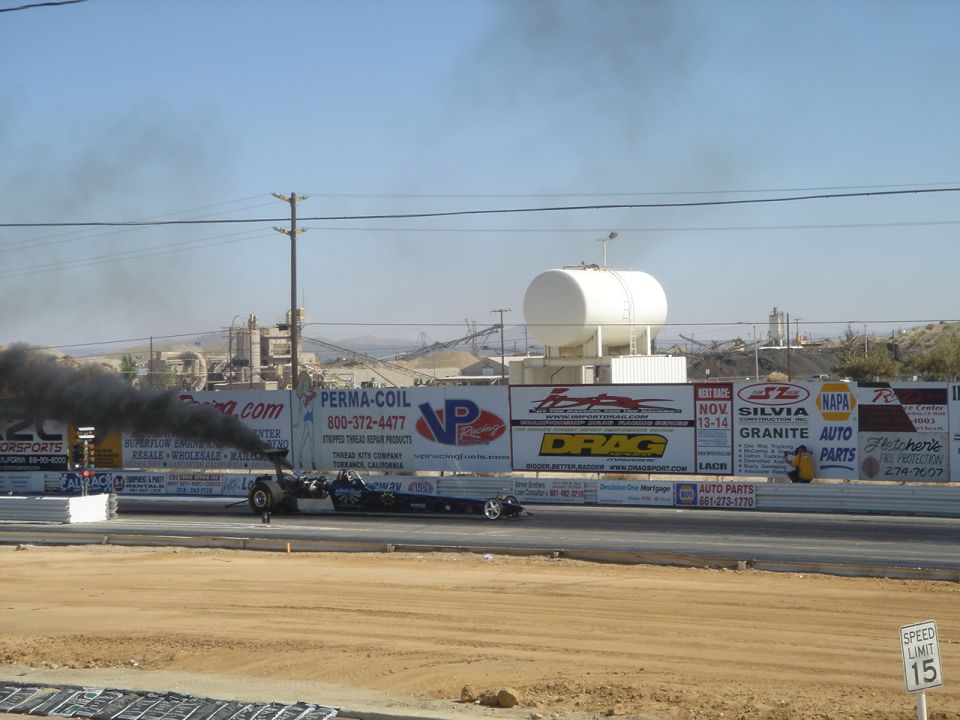 Dragster side view emitting black smoke on a drag strip