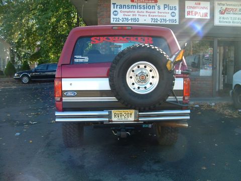 1994 Ford Bronco - The rear of a red Ford Bronco is shown parked in front of a repair shop. A spare tire is mounted on the back.