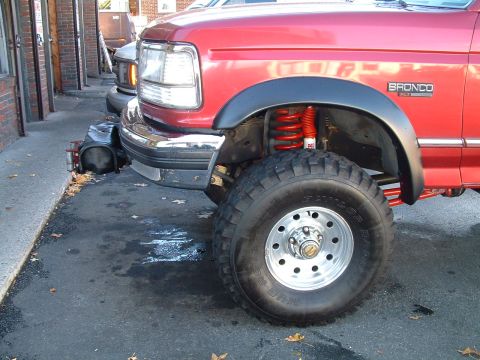 1994 Ford Bronco - A red Ford Bronco with a lifted suspension and off-road tires is parked on an asphalt surface.