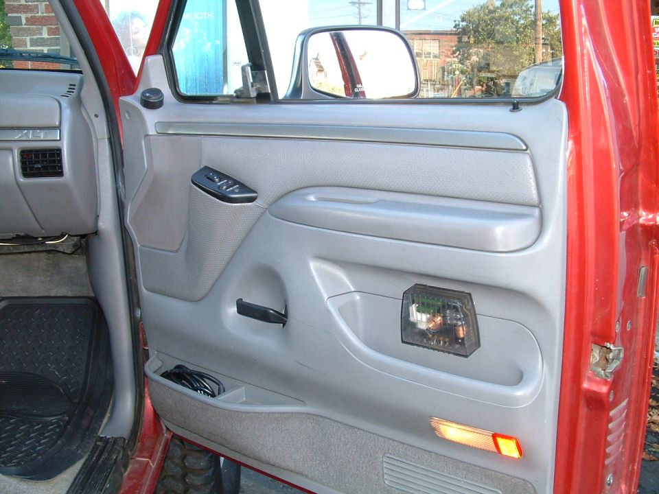 Gray interior door panel of red Ford with window crank and power switches, door open outdoors