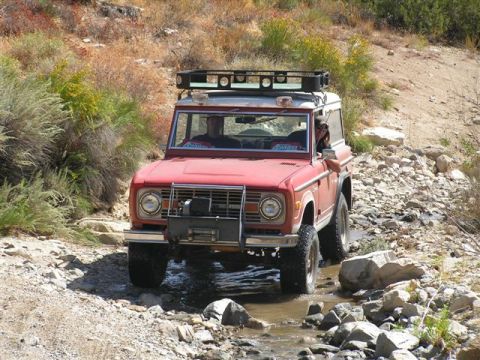 1988 Ford Bronco - A red 1978 Ford Bronco navigates a rocky stream in a dry, brushy landscape.