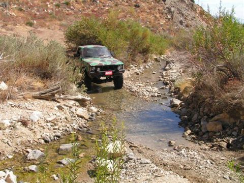 1988 Ford Bronco - A pickup truck with camouflage paint navigates a rocky, dry creek bed in a desert-like environment.