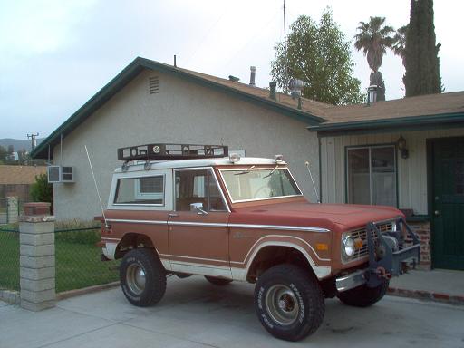 Red and white 1973 Ford Bronco with roof rack and winch parked in driveway