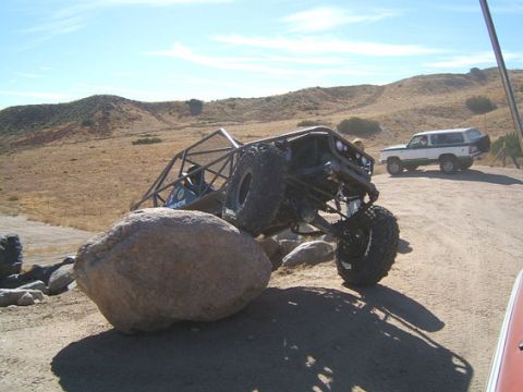 1973 Ford Bronco - A custom-built off-road vehicle navigates a rocky terrain, with another vehicle visible in the background under a clear sky.