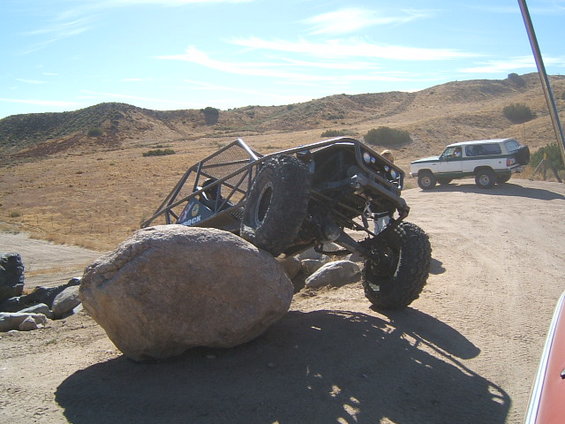 Custom buggy with roll cage is on large rocks, another SUV is parked behind it