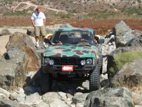 1973 Ford Bronco - A camouflage pickup truck is shown off-roading through a rocky terrain.