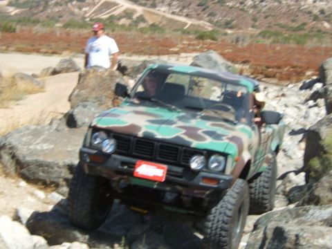 1973 Ford Bronco - A camouflage pickup truck is shown off-roading over large rocks.