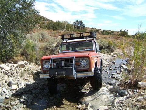 1973 Ford Bronco - 1973 Ford Bronco off-roading on a rocky trail with a stream.