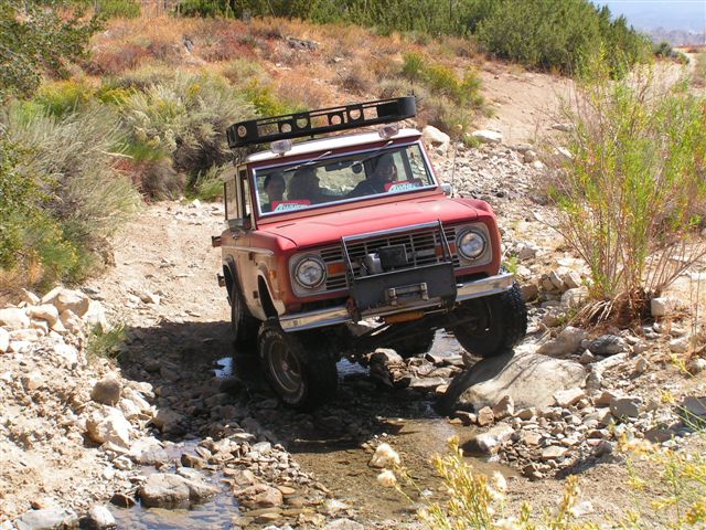Red 1973 Ford Bronco navigating rocky terrain with water crossing