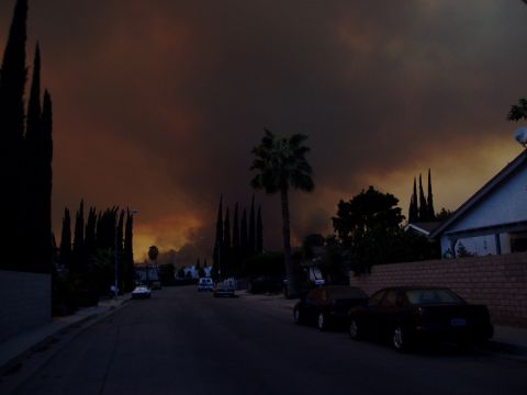 1995 Ford Taurus - A residential street is shrouded in smoke from a distant fire, casting an ominous glow on the sky.