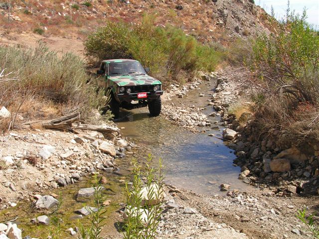 Camouflage pickup truck driving through a rocky stream bed