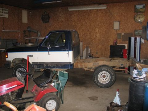 1989 Ford F-150 - A 1989 Ford F-150 flatbed truck is seen from the side, parked inside a garage.