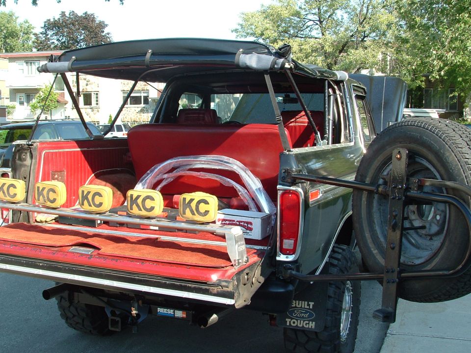 Dark green 1978 Ford Bronco rear view with spare tire carrier, red interior, and KC lights