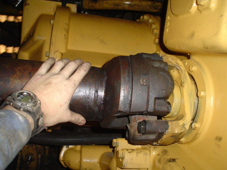 Hand touching rusty driveshaft and yellow machinery component