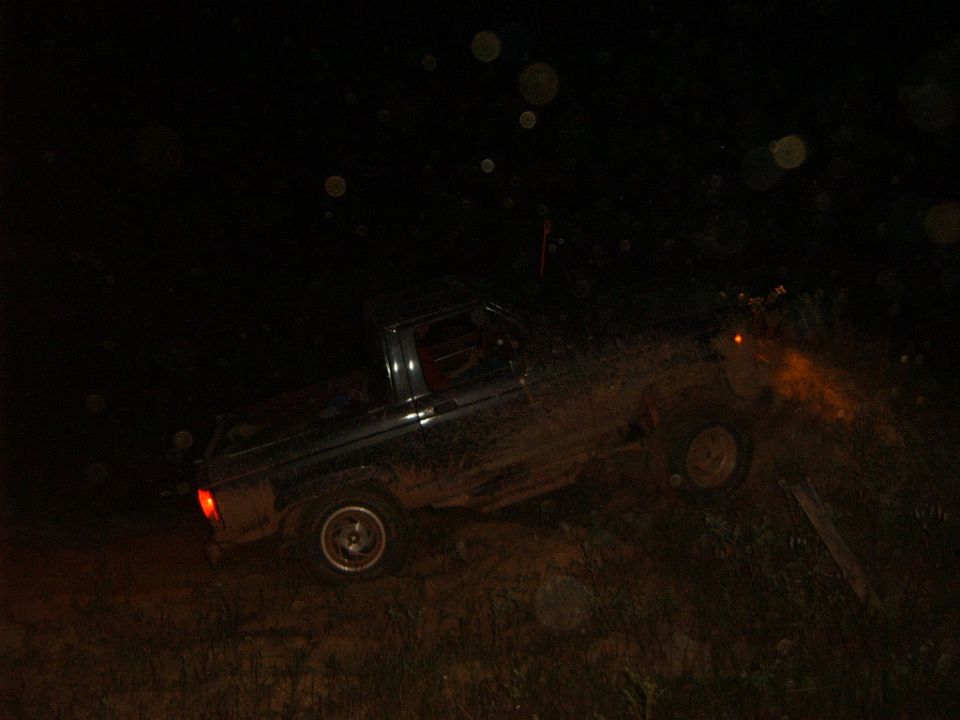 Dark blue Ford Bronco II driving off-road at night, covered in mud