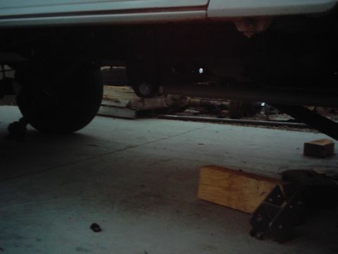 1978 Ford Bronco - The underside of a vehicle is visible, showing its chassis, a large tire, and wooden blocks supporting it.