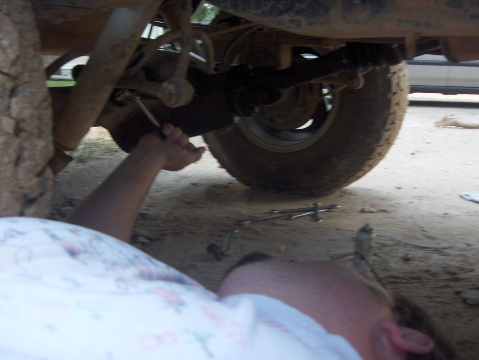 Person's arm and hand using a wrench on the underside of a vehicle, near the rear tire