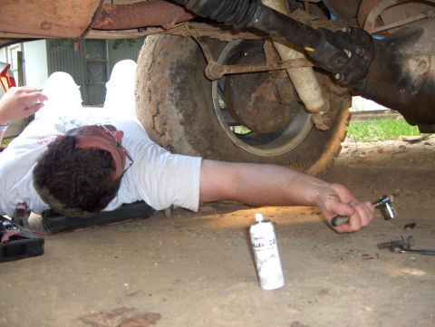 1985 Ford Bronco II - A person works on the underside of a vehicle, with a drive shaft and rear axle visible.