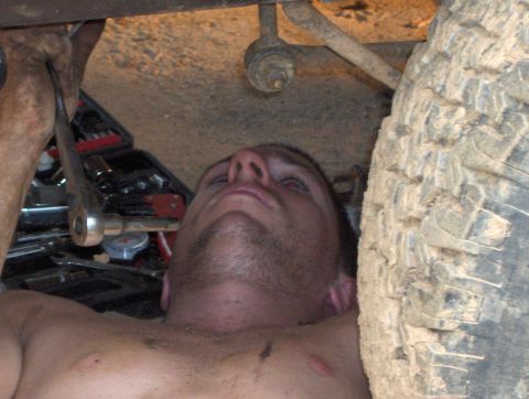 1985 Ford Bronco II - A mechanic is seen working on the underside of a vehicle, with a large tire in the foreground.