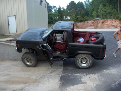 1985 Ford Bronco II - A black 1985 Ford Bronco II is parked outside a building with its doors open and a spare tire visible in the cargo area.