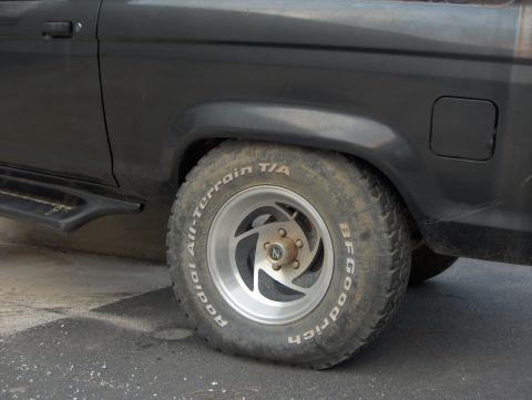 1985 Ford Bronco II - The side profile of a black 1985 Ford Bronco II is visible, focusing on the rear wheel and fender area with BFGoodrich tires.
