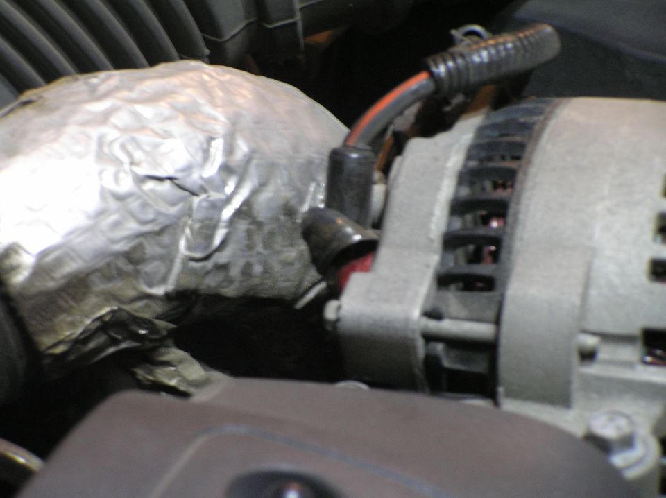 Gray alternator beside foil heat-shielded engine component with black wiring