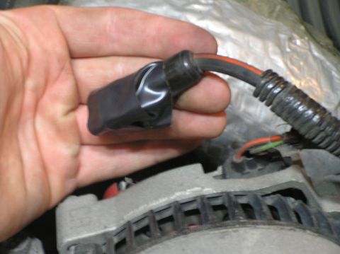 2000 Ford Excursion - A hand holds a taped wiring harness connector near an alternator, likely during a repair or replacement.
