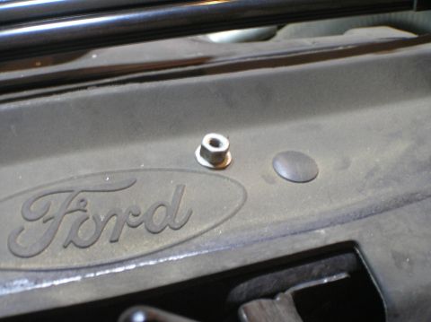 2000 Ford Excursion - A close-up view of the Ford logo on a vehicle's engine cover, showing a fastener.
