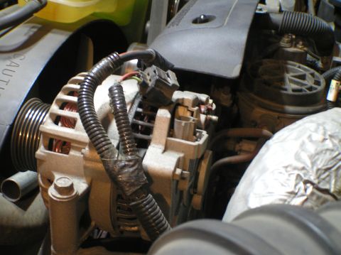 2000 Ford Excursion - Close-up view of an alternator within an engine compartment, showing electrical connections and a pulley.